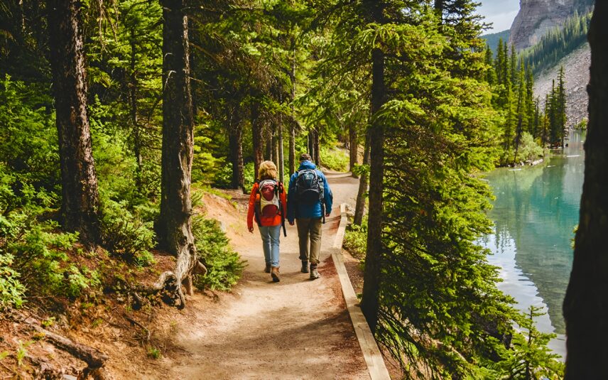 A couple hiking through a shaded pathway beside a lake.
