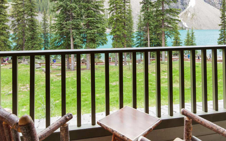 Two chairs on a balcony overlooking Moraine Lake, with scenic views of the turquoise water and surrounding trees, offering a tranquil and picturesque setting.