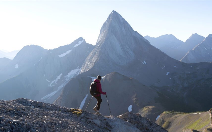 A hiker scaling down a mountain with snowcapped mountains in the distance.