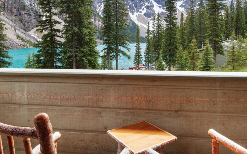 Two chairs on a balcony overlooking Moraine Lake, with scenic views of the turquoise water and surrounding trees, offering a tranquil and picturesque setting.