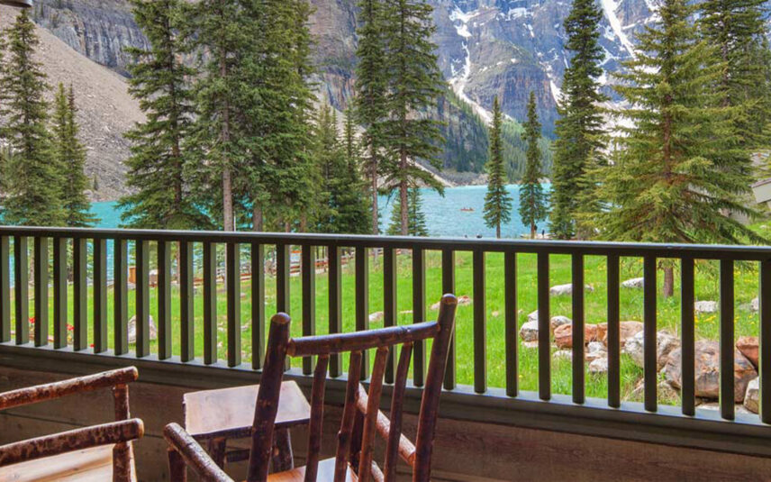 Two chairs on a balcony overlooking Moraine Lake, with scenic views of the turquoise water and surrounding trees, offering a tranquil and picturesque setting.