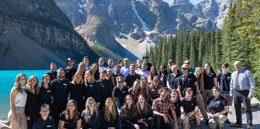 A group photo of team members working at Moraine Lake Lodge, smiling together in a friendly and welcoming pose, with the natural beauty of the surrounding mountains and lake in the background.