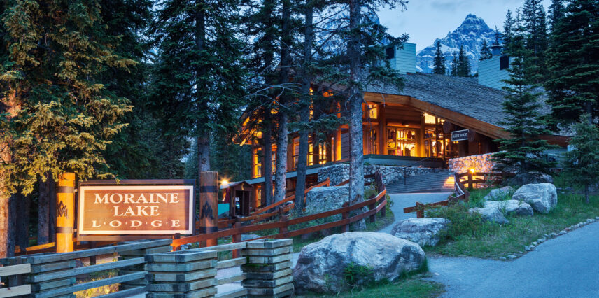 The entrance to Moraine Lake Lodge at dusk, with soft lighting illuminating the rustic architecture, set against the backdrop of the fading sky and surrounding natural beauty.