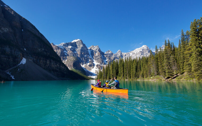A family of three paddling in a yellow canoe on Moraine Lake, surrounded by vibrant turquoise waters and majestic mountains, enjoying a peaceful outdoor adventure.