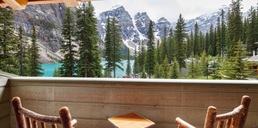 Two chairs on a balcony overlooking Moraine Lake, with scenic views of the turquoise water and surrounding trees, offering a tranquil and picturesque setting.